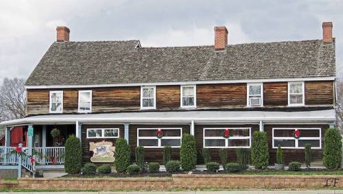 A rustic two-story wooden house decorated with holiday wreaths and greenery, featuring a porch and a sign.