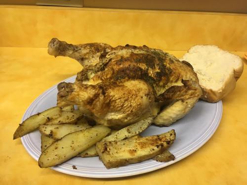 A roasted chicken on a plate with seasoned potato wedges and a slice of bread on a yellow countertop.