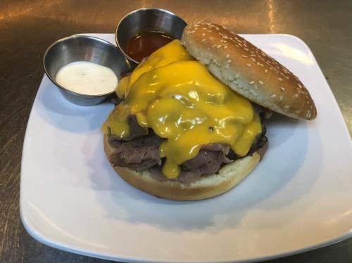 A sesame seed bun filled with roast beef and melted cheddar cheese, served with two dipping sauces on the side.