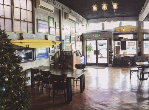 Cozy café interior with a Christmas tree, surfboards, artwork on the walls, and large windows letting in natural light.