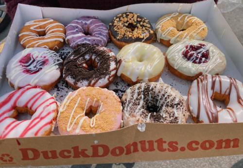 A box of assorted donuts with various colorful glazes and toppings, including sprinkles and drizzles.