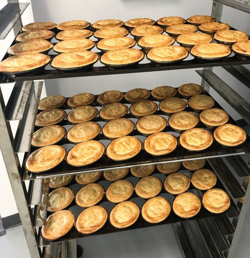 A rack filled with multiple trays of golden-brown baked pies, neatly arranged in three rows.