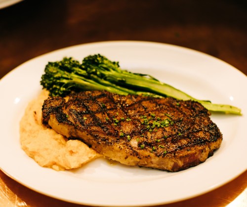 A grilled steak on a plate, served with creamy mashed potatoes and sautéed broccolini.