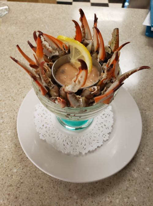 A glass dish filled with crab claws arranged around a small bowl of sauce, garnished with a lemon slice.
