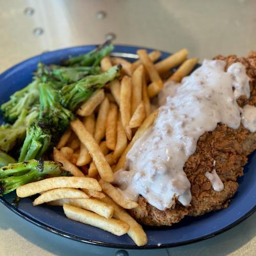 A plate of fried chicken topped with gravy, served with French fries and steamed broccoli.