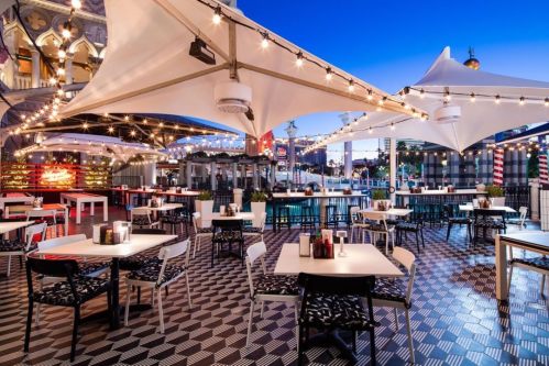 Outdoor restaurant patio with string lights, tables, and chairs, set against a twilight skyline.