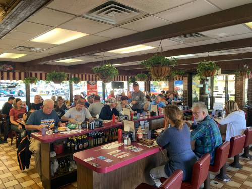 A busy diner filled with patrons sitting at the counter and tables, enjoying meals and chatting in a cozy atmosphere.