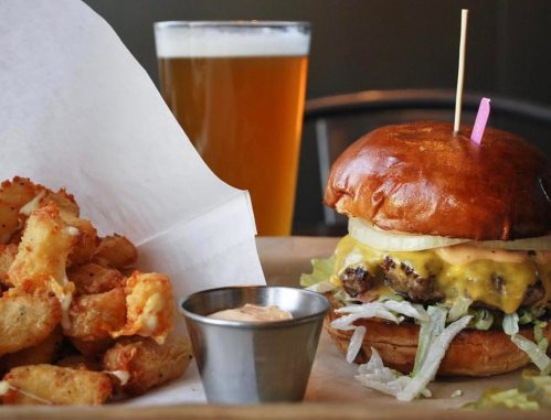 A juicy cheeseburger with lettuce and onion, served with crispy potato wedges and a pint of beer.