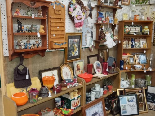 A display of various vintage items, including glassware, figurines, and decorative pieces on wooden shelves.