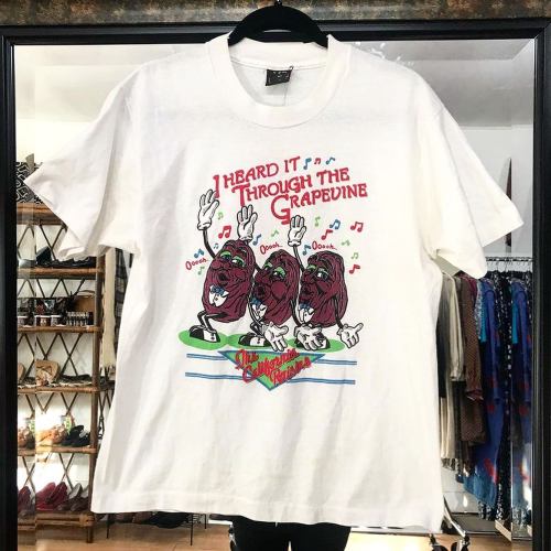 A white t-shirt featuring three cartoon grapes singing with the text "I Heard It Through The Grapevine."