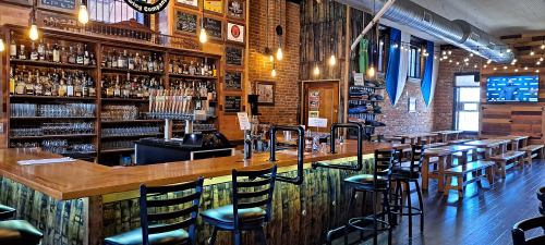 A rustic bar with wooden decor, shelves of liquor, and a row of empty stools in a cozy, well-lit setting.