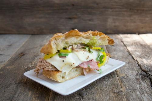 A hearty sandwich with pulled pork, melted cheese, and green peppers on a crusty roll, served on a white plate.