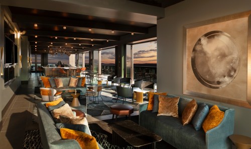 Modern lounge with stylish furniture, large windows, and a sunset view, featuring warm colors and elegant decor.