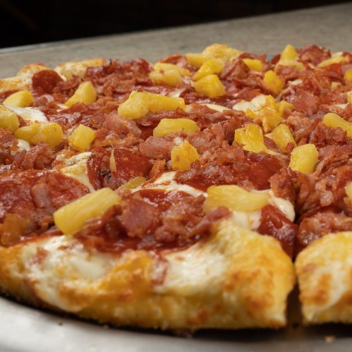A close-up of a pizza topped with pepperoni, ham, pineapple, and melted cheese on a golden crust.
