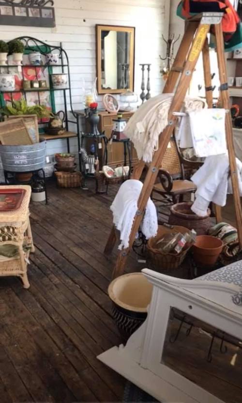 A cozy vintage shop interior filled with various decor items, baskets, and a wooden ladder displaying textiles.