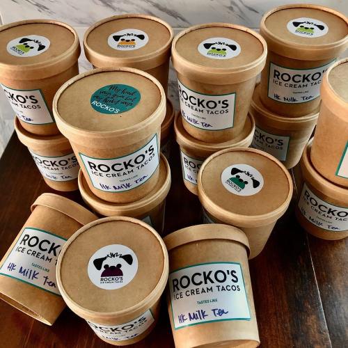 A collection of round, brown ice cream containers labeled "Rocko's Ice Cream Tacos" with various flavors.