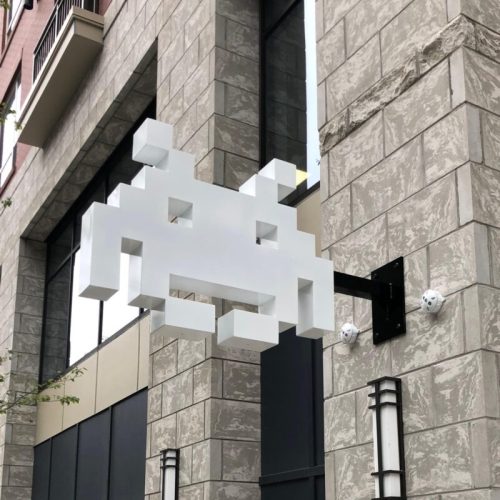 A pixelated white space invader sign mounted on a stone building exterior.