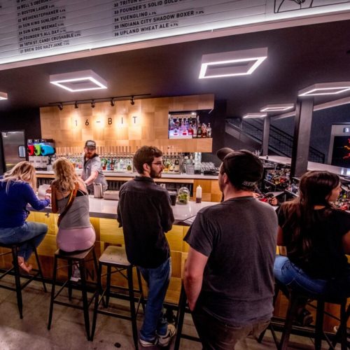 A lively bar scene with patrons enjoying drinks at a modern bar featuring a variety of beverages and a bartender.
