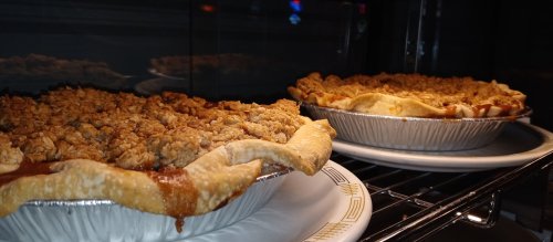 Two freshly baked pies with crumbly topping, cooling on a rack in an oven.
