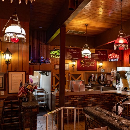 Cozy restaurant interior with wooden walls, vintage lighting, and a counter displaying menu items and drinks.