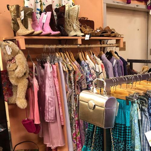 A display of vintage clothing, including dresses, boots, and accessories, in a colorful thrift store setting.