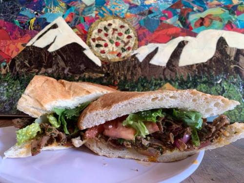 A close-up of a sandwich filled with lettuce, tomato, and meat, set against a colorful mountain-themed background.