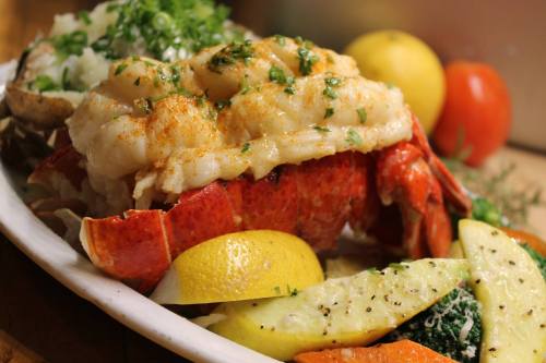 A plate of lobster tail with lemon, garnished with herbs, alongside mixed vegetables and a side of rice.