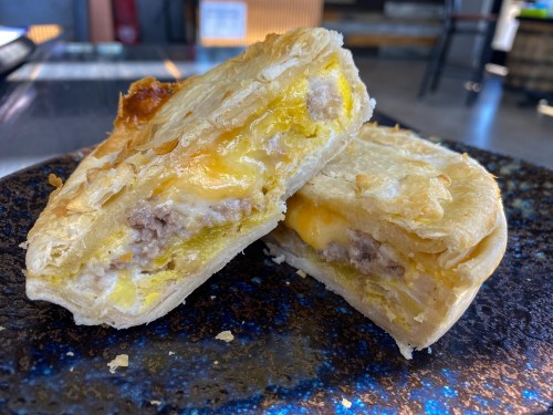 A close-up of a flaky pastry filled with meat and cheese, cut in half to reveal its golden interior.