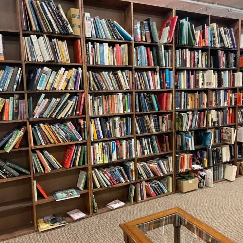 A wooden bookshelf filled with a variety of books in different colors and sizes, with a glass-topped table in front.
