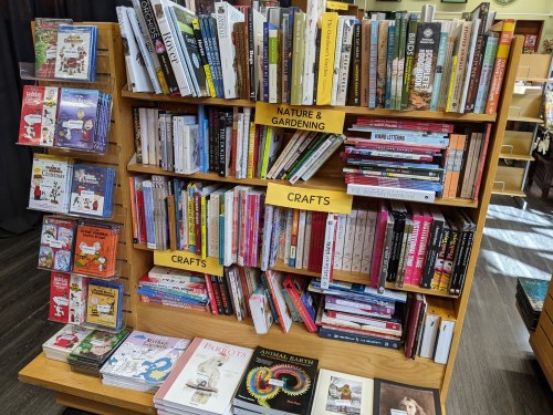 A wooden bookshelf filled with various books on crafts, nature, gardening, and related topics, with colorful covers.