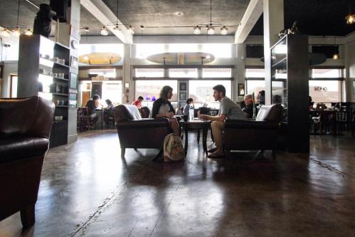 Two people sit across from each other in a cozy café, engaged in conversation, surrounded by other patrons.