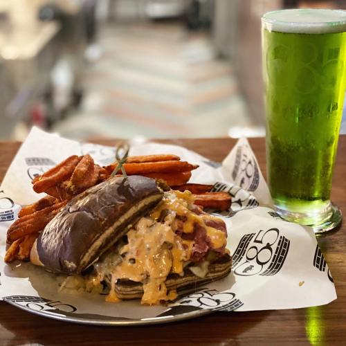 A hearty burger with melted cheese and toppings, served with sweet potato fries and a green drink on the side.