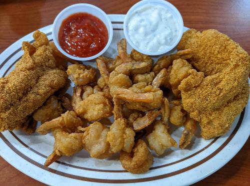 A plate of fried shrimp and fish, served with two dipping sauces: one red and one white.