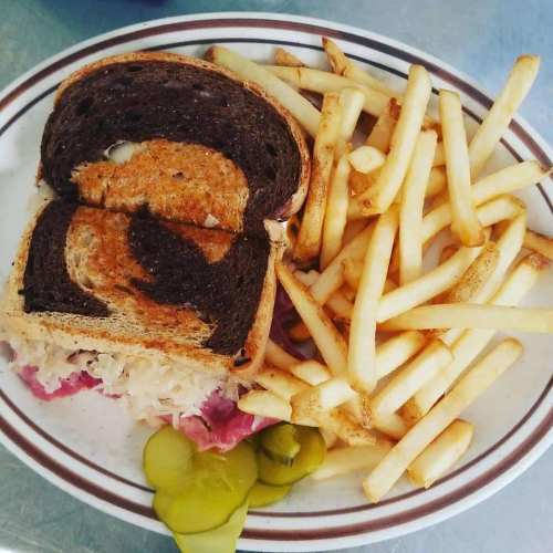 A plate with a sandwich on dark bread, sauerkraut, pickles, and a side of golden French fries.