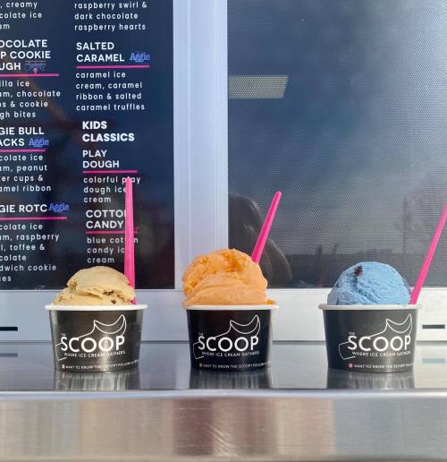 Three ice cream cups in front of a menu, featuring flavors like salted caramel, orange, and blue cotton candy.