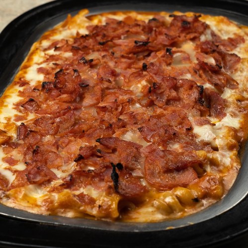 A close-up of a baked dish topped with crispy bacon, melted cheese, and a golden crust on a black serving tray.
