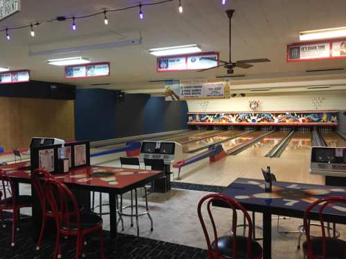 Interior of a bowling alley featuring lanes, seating, and colorful decor. Bright lights and a casual atmosphere.