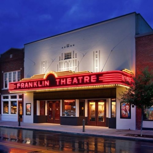 The Franklin Theatre illuminated at night, showcasing its marquee and art deco architecture.