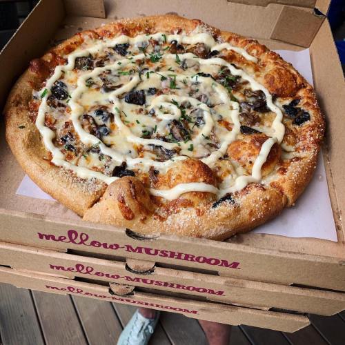 A freshly baked pizza topped with mushrooms, cheese, and a swirl of sauce, resting in a pizza box.