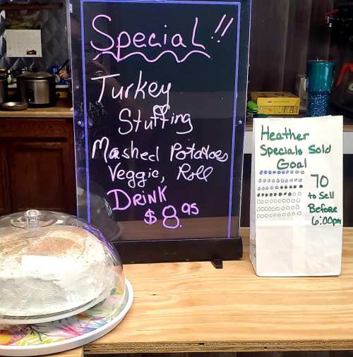 A chalkboard sign lists a special meal: turkey stuffing, mashed potatoes, veggie, roll, and drink for $8.95. A cake is displayed nearby.