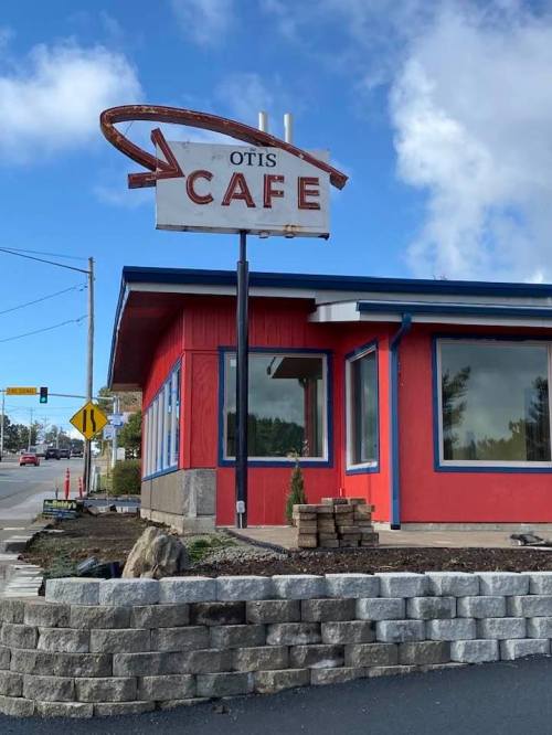 A red cafe building with a retro sign reading "Otis Cafe" against a blue sky and nearby road.