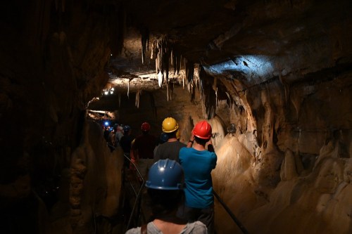 A group of people wearing helmets explores a cave with stalactites and dim lighting.