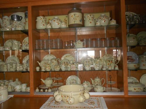 A display cabinet filled with vintage cream-colored dishware featuring floral patterns, including teapots and serving dishes.