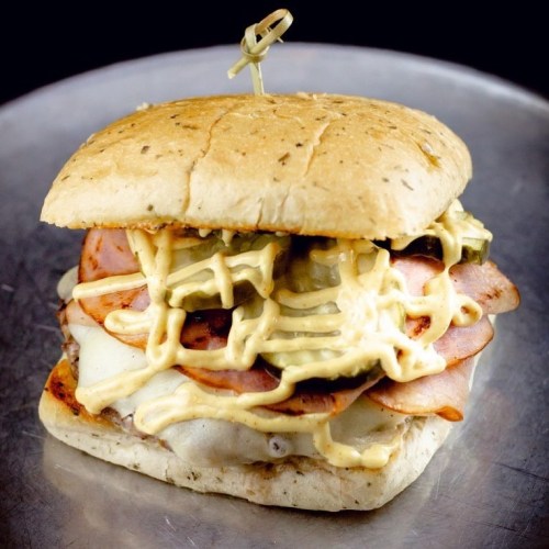 A hearty sandwich with layers of ham, cheese, pickles, and drizzled with sauce, served on a toasted bun.