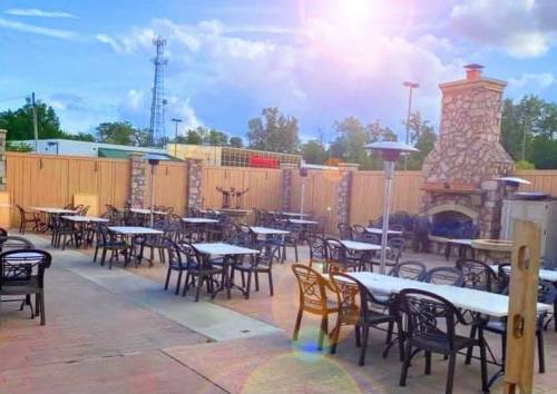Outdoor patio with tables and chairs, a stone fireplace, and a sunny sky in the background.