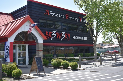 Exterior of a brewery with a red roof, sign reading "Brewery Hocking Hills," and an open flag in front.