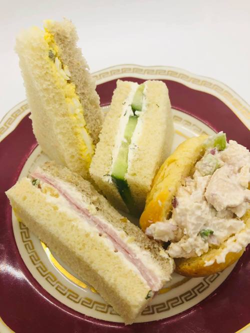 A plate with four assorted sandwiches: egg, cucumber, ham, and chicken salad on soft white bread.