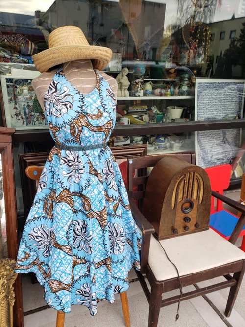 A vibrant blue patterned dress on a mannequin, with a straw hat, beside vintage decor and an old radio.