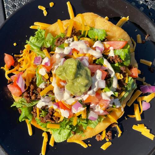 A colorful taco salad with ground beef, lettuce, tomatoes, cheese, onions, and guacamole on a crispy shell.