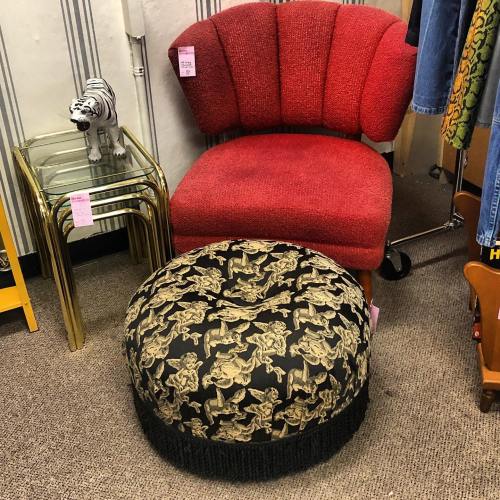 A red vintage chair next to a black pouf with gold patterns, set in a retro-styled room with various decor items.